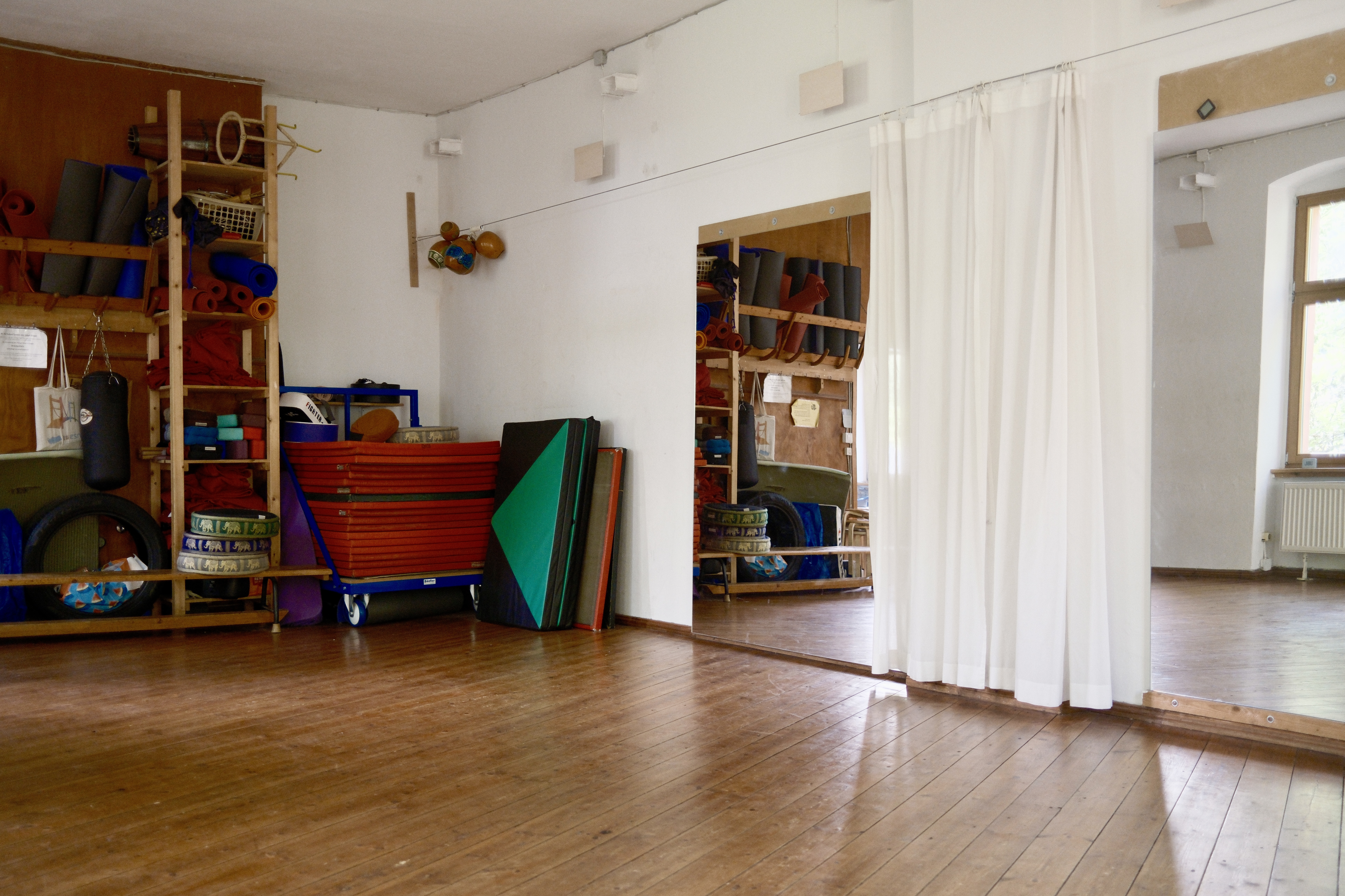 Ein heller großer Raum mit einem großen Regal mit Matten an der Wand und einem großen Spiegel